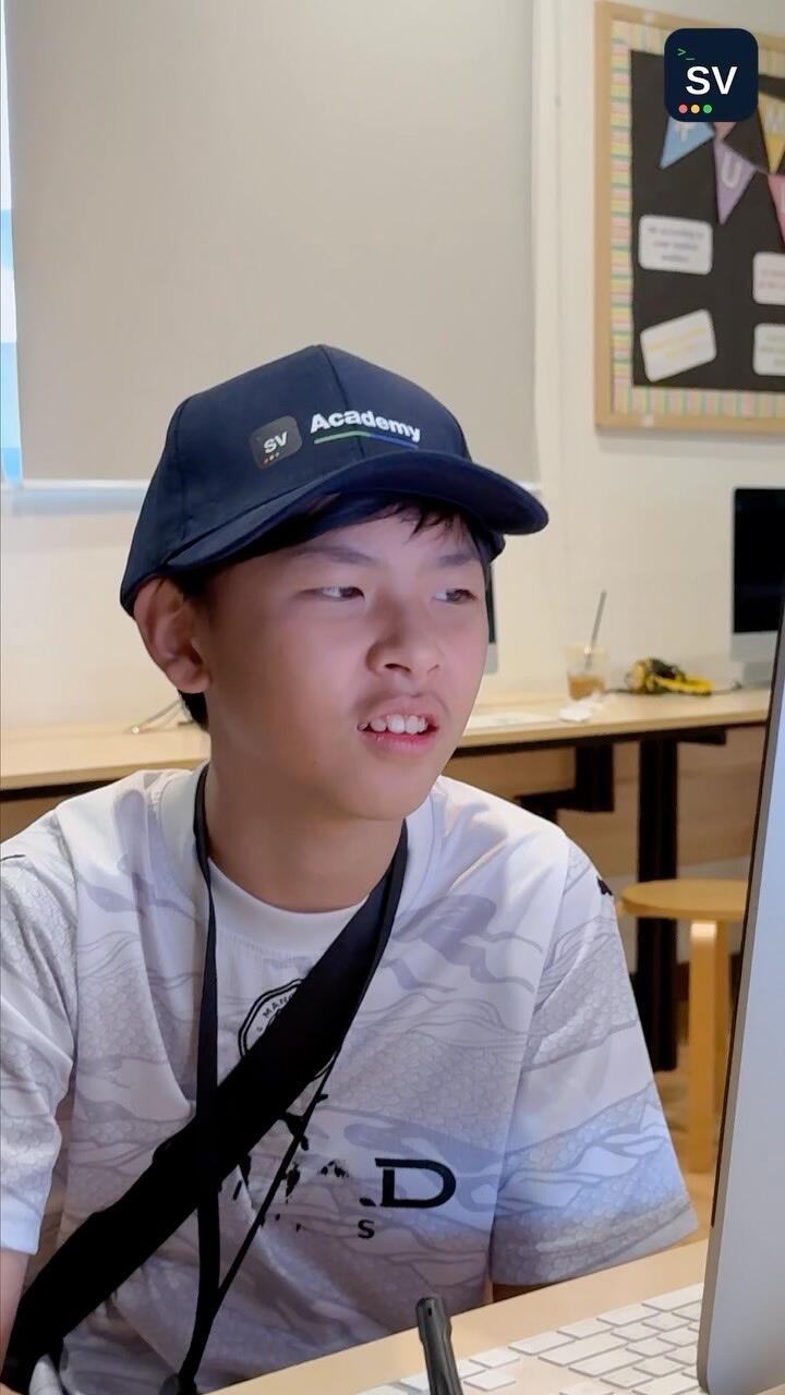A boy in an SV Academy cap looks at an iMac screen in a classroom
