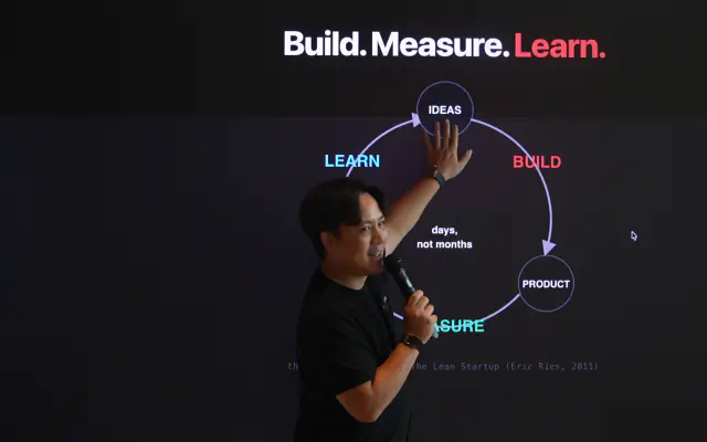 A mentor on stage in front of a Build, Measure, Learn slide