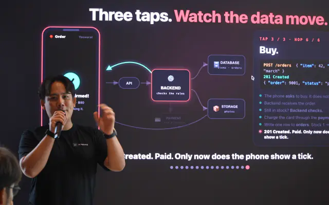 A mentor on stage explaining how an app moves data, with a live diagram behind him