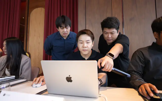 Business owners gathered around one laptop as a mentor points at the screen